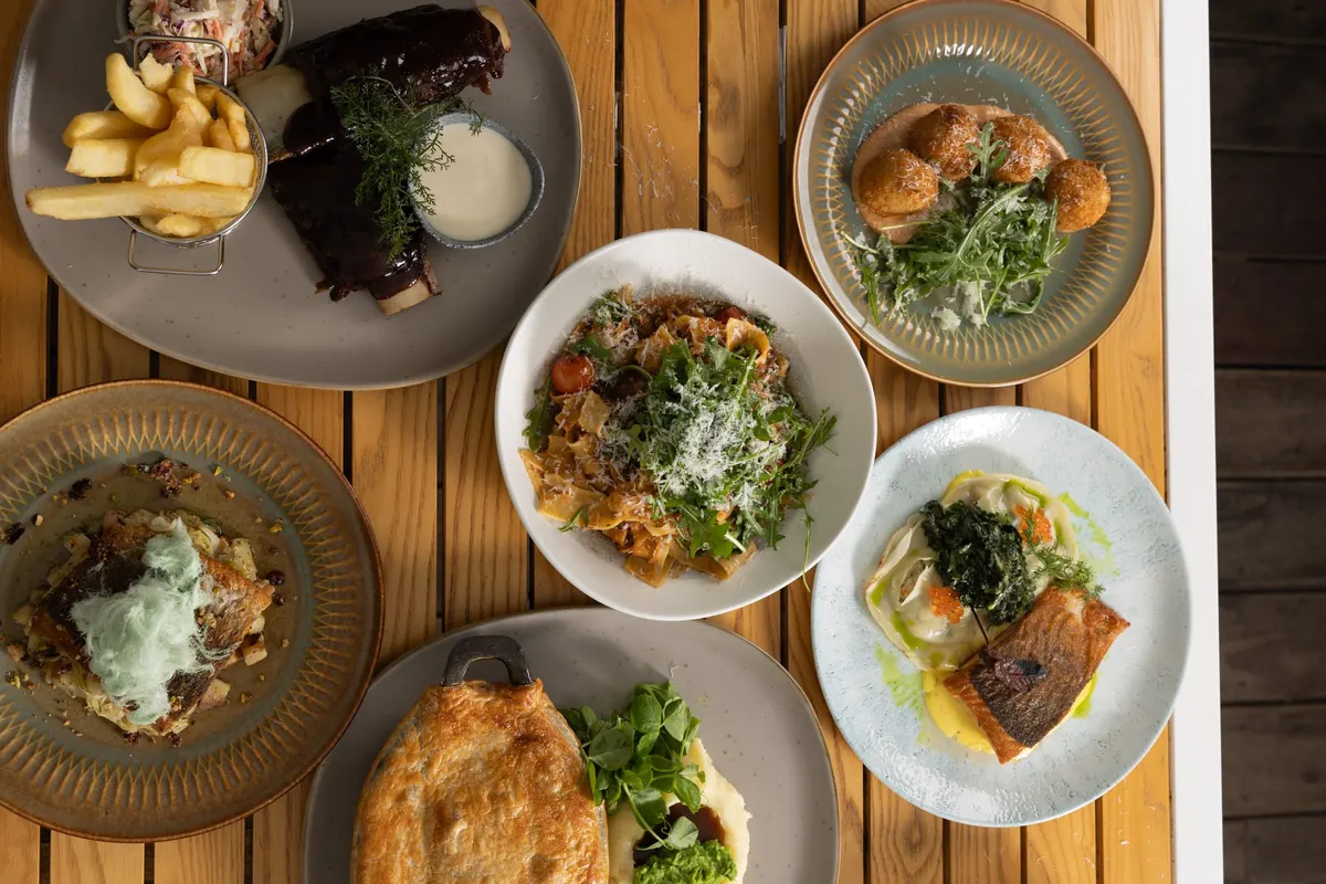 Shared plates of chips, salads and grilled mains on a timber table