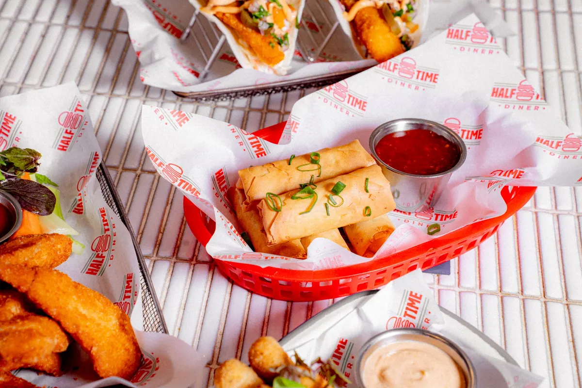 Spring rolls, chicken and dipping sauces in a red diner basket