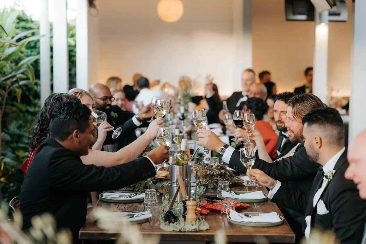 Wedding guests raising glasses at a long dinner table