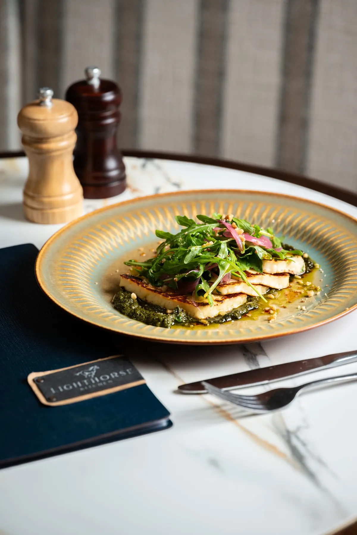 Grilled halloumi on pesto with rocket, on a gold-rimmed plate