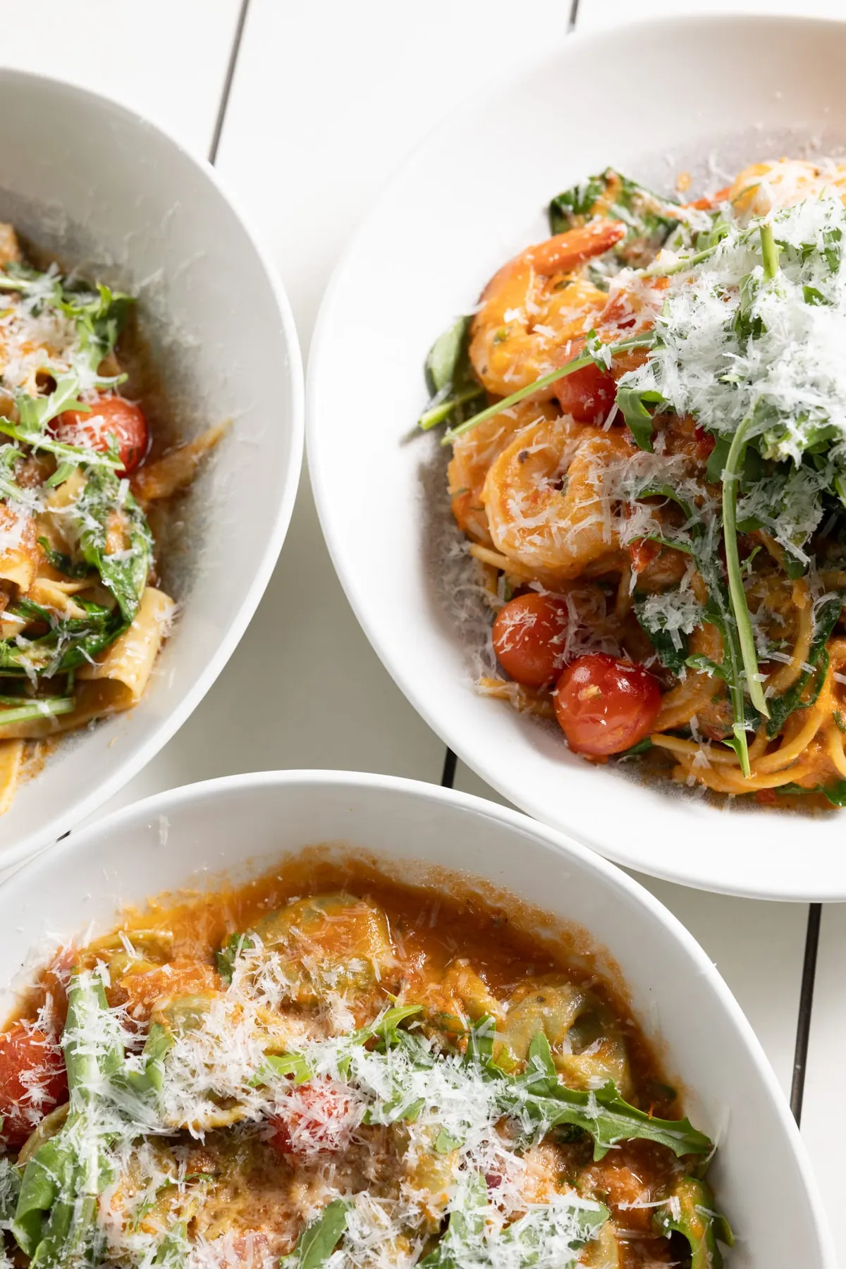 Bowls of prawn pasta and salad topped with shaved parmesan