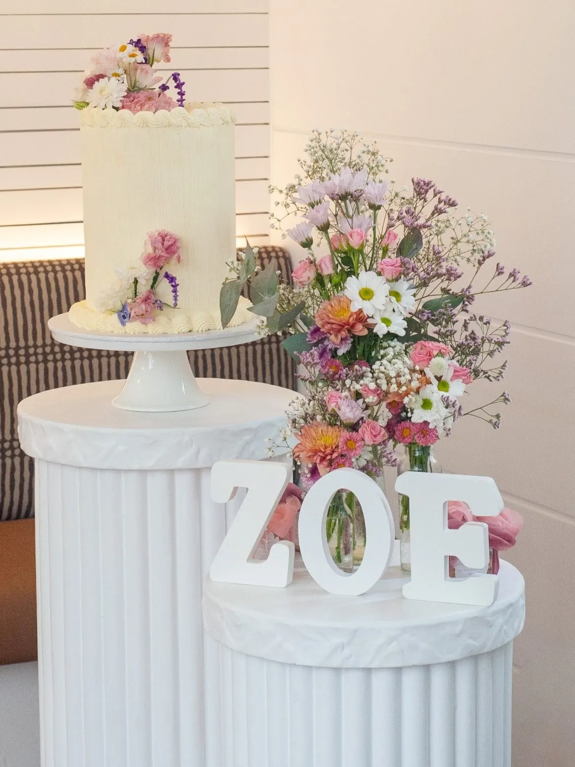 Birthday cake with fresh flowers beside the name ZOE on white pedestals