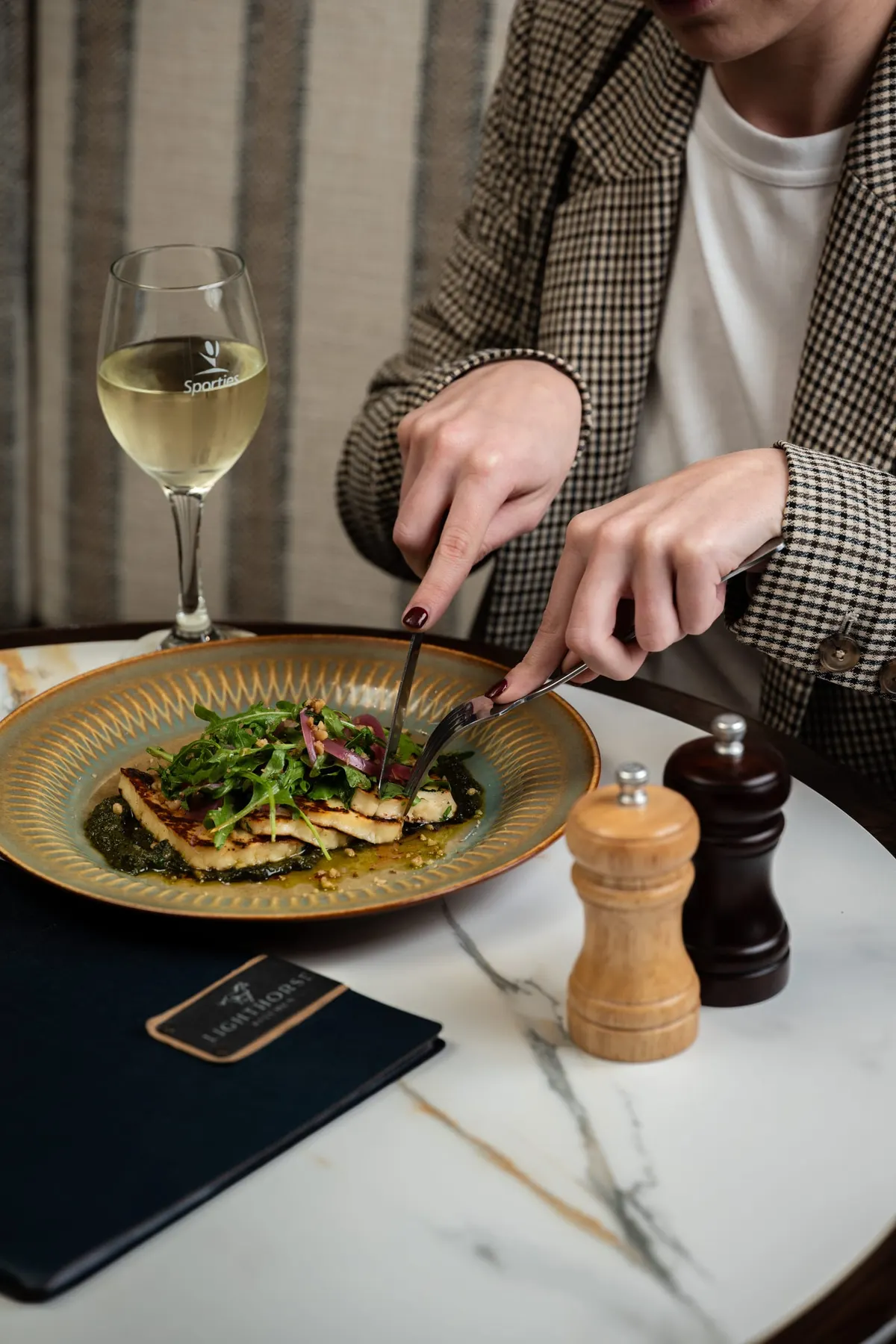 Guest cutting into a plated main beside a glass of white wine
